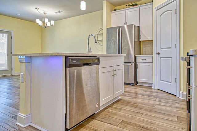 kitchen featuring an island with sink, stainless steel appliances, light countertops, white cabinetry, and pendant lighting