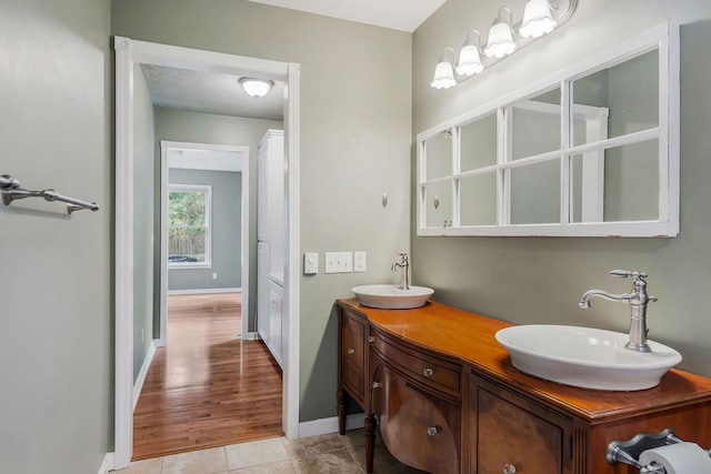 bathroom featuring double vanity, tile patterned flooring, a sink, and baseboards