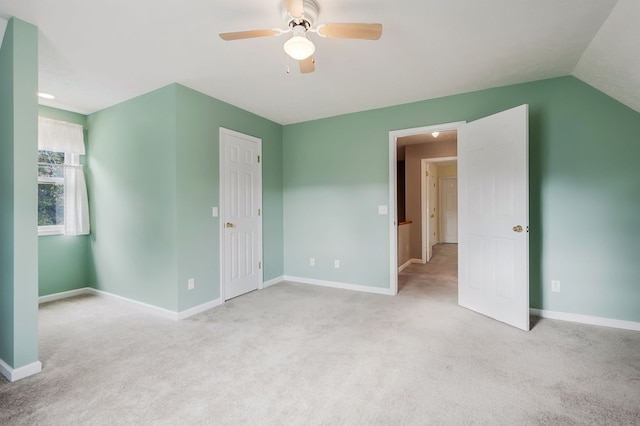 interior space featuring lofted ceiling, ceiling fan, baseboards, and light colored carpet