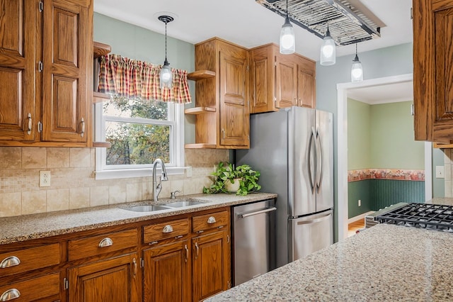 kitchen with brown cabinetry, light stone counters, pendant lighting, and a sink