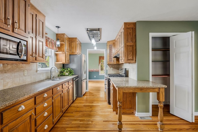 kitchen featuring appliances with stainless steel finishes, brown cabinetry, a sink, and hanging light fixtures