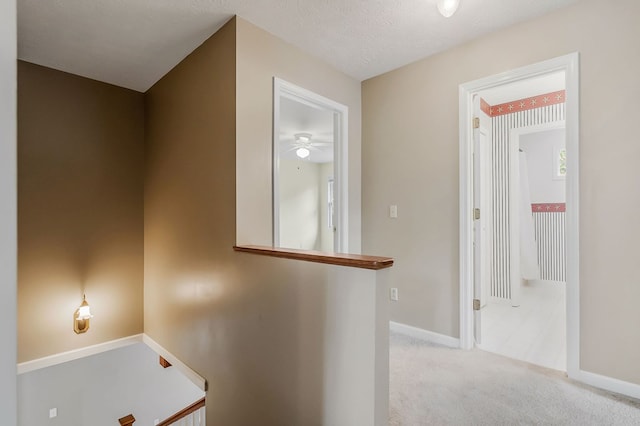 corridor with a textured ceiling, carpet, an upstairs landing, and baseboards