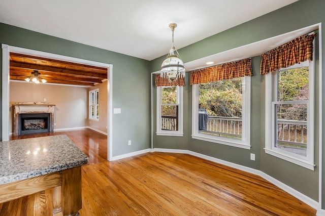 unfurnished dining area featuring light wood-type flooring, a fireplace, baseboards, and ceiling fan with notable chandelier