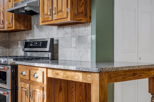 kitchen with under cabinet range hood, tasteful backsplash, range with two ovens, and brown cabinetry