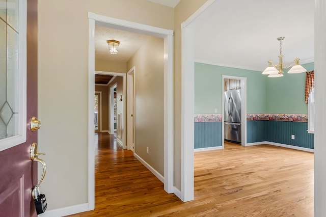 hallway with wallpapered walls, baseboards, wainscoting, wood finished floors, and a textured ceiling