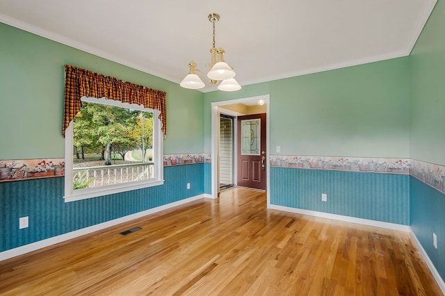 empty room with a notable chandelier, visible vents, wainscoting, wood finished floors, and wallpapered walls