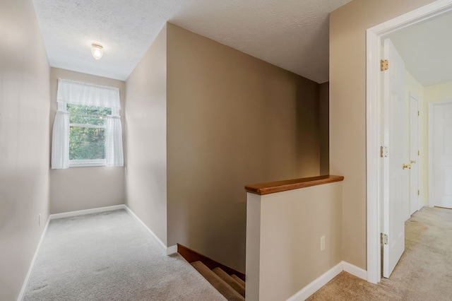 hallway featuring light carpet, a textured ceiling, and an upstairs landing