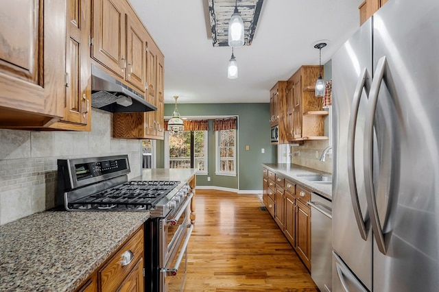 kitchen featuring light stone countertops, under cabinet range hood, pendant lighting, and stainless steel appliances