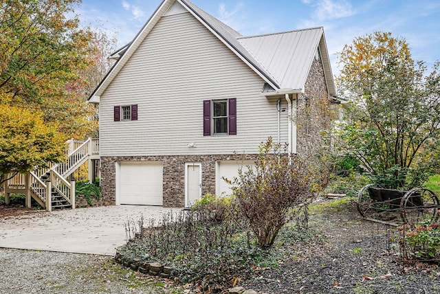 view of side of property with a garage, stone siding, stairway, and driveway