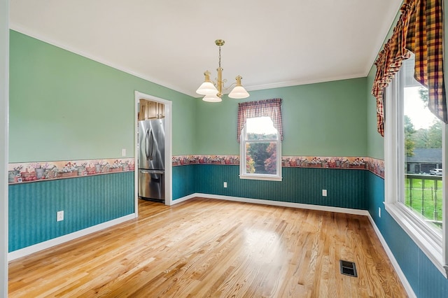 unfurnished room featuring a wainscoted wall, wood finished floors, visible vents, and wallpapered walls