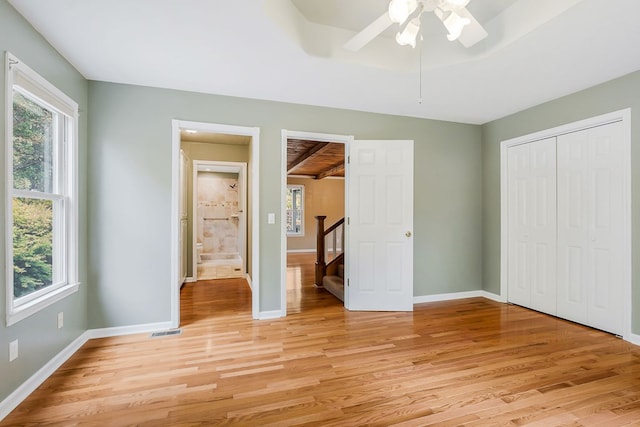 unfurnished bedroom featuring visible vents, multiple windows, a raised ceiling, and light wood-style flooring