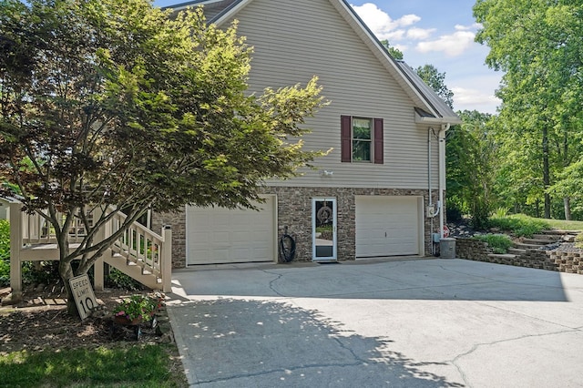 view of side of home with a garage, stone siding, concrete driveway, and stairs