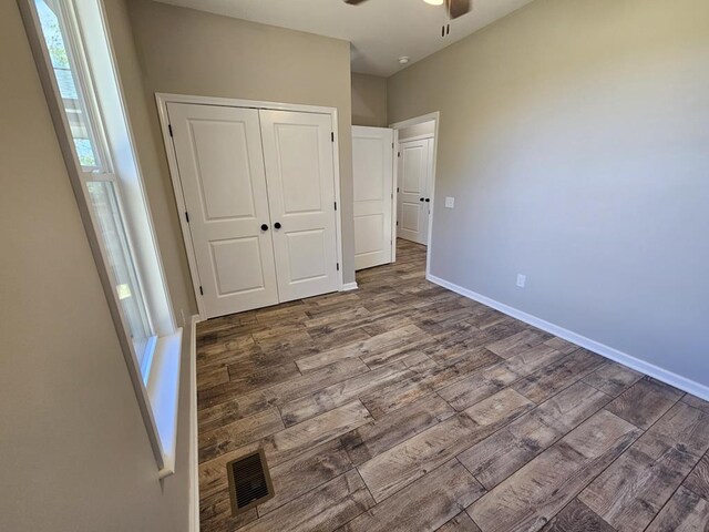 unfurnished bedroom featuring a closet, visible vents, a ceiling fan, wood finished floors, and baseboards