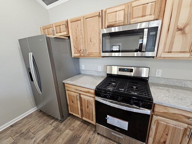 kitchen featuring baseboards, appliances with stainless steel finishes, wood finished floors, light stone countertops, and light brown cabinets