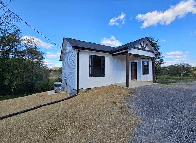 view of front facade with crawl space, roof with shingles, a patio, and central air condition unit