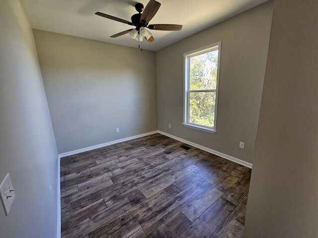 spare room featuring dark wood-style flooring, a ceiling fan, and baseboards