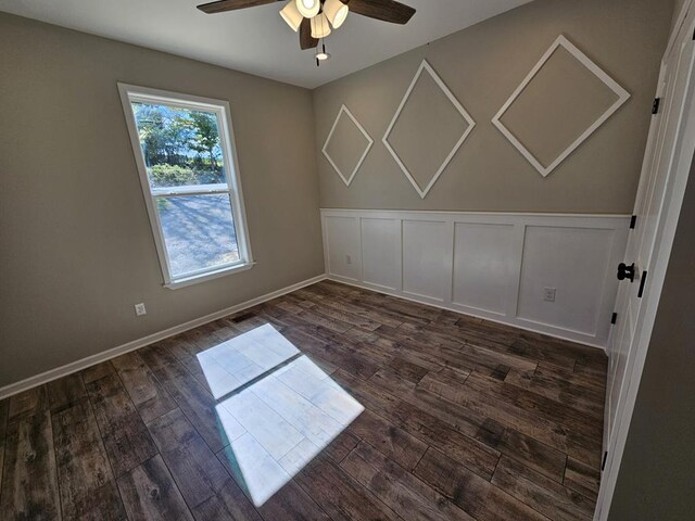 spare room with baseboards, dark wood finished floors, a ceiling fan, and a decorative wall