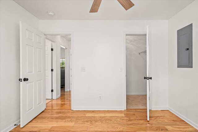 unfurnished bedroom featuring a walk in closet, a closet, electric panel, and light wood finished floors