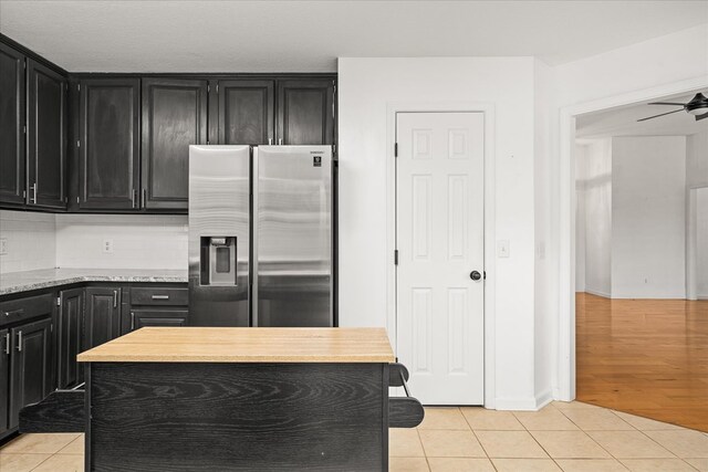 kitchen featuring light tile patterned floors, dark cabinetry, stainless steel refrigerator with ice dispenser, and tasteful backsplash