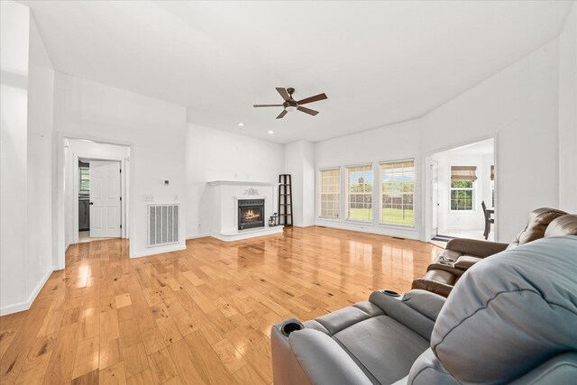 living room featuring a warm lit fireplace, light wood-type flooring, visible vents, and baseboards