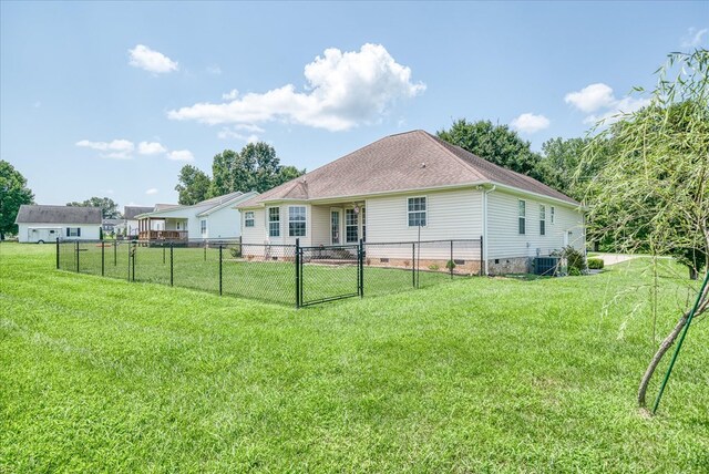 rear view of house featuring roof with shingles, crawl space, fence private yard, and a lawn