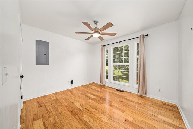 empty room with electric panel, baseboards, visible vents, ceiling fan, and light wood-style floors