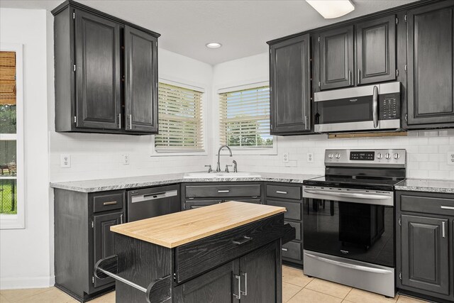 kitchen featuring light tile patterned floors, backsplash, appliances with stainless steel finishes, a sink, and dark cabinetry