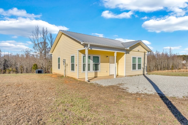 back of house with driveway, metal roof, and a yard