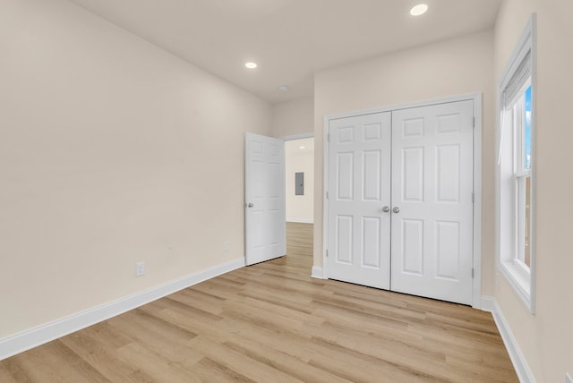 unfurnished bedroom with recessed lighting, baseboards, a closet, light wood-type flooring, and electric panel