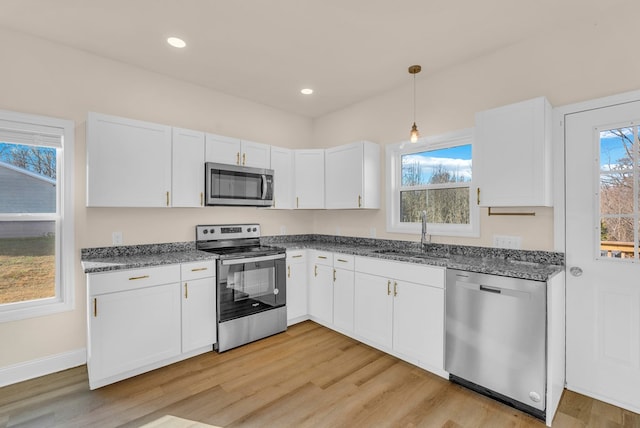 kitchen featuring light wood finished floors, stainless steel appliances, white cabinets, a sink, and plenty of natural light