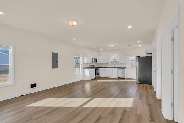 kitchen featuring light wood finished floors, stainless steel appliances, white cabinets, electric panel, and baseboards