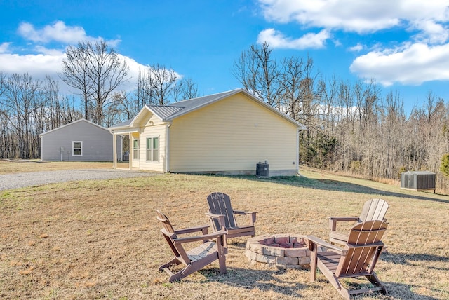 view of property exterior featuring a fire pit, metal roof, central AC unit, and a lawn