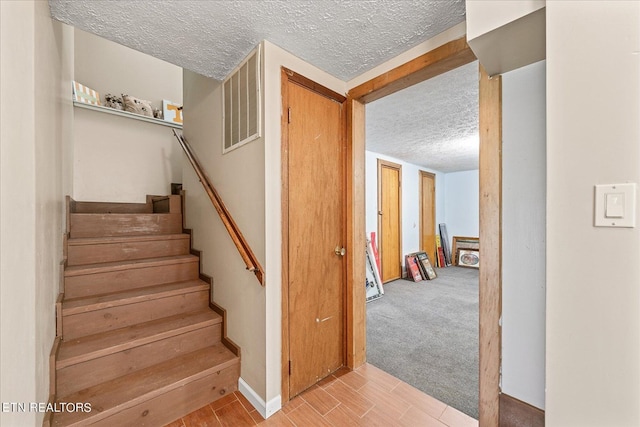 staircase with visible vents, a textured ceiling, and wood finished floors