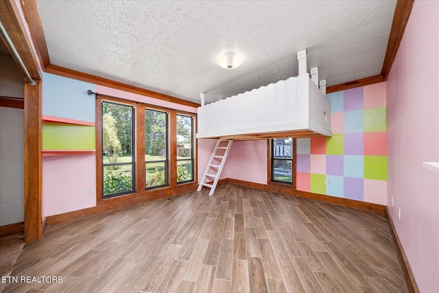 interior space with wallpapered walls, a textured ceiling, baseboards, and wood finished floors