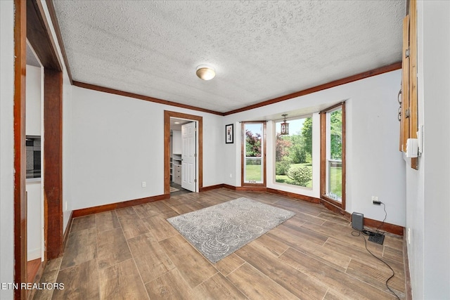 empty room with a textured ceiling, ornamental molding, wood finished floors, and baseboards