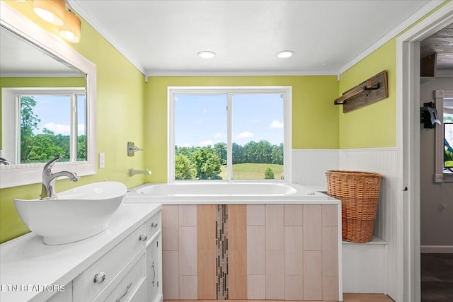 bathroom featuring a garden tub, recessed lighting, vanity, wainscoting, and crown molding