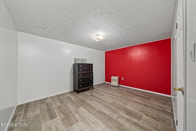 empty room featuring a textured ceiling, an accent wall, baseboards, and wood finished floors