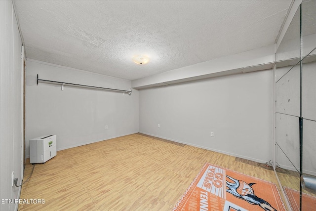 basement featuring a textured ceiling, baseboards, and wood finished floors