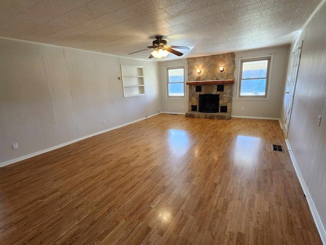 unfurnished living room with a wealth of natural light, visible vents, wood finished floors, and a stone fireplace