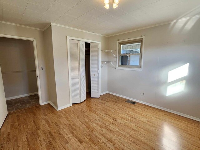 unfurnished bedroom with visible vents, baseboards, light wood-style floors, a closet, and crown molding