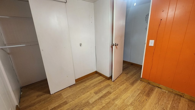 unfurnished bedroom with light wood-style floors, a closet, and wood walls