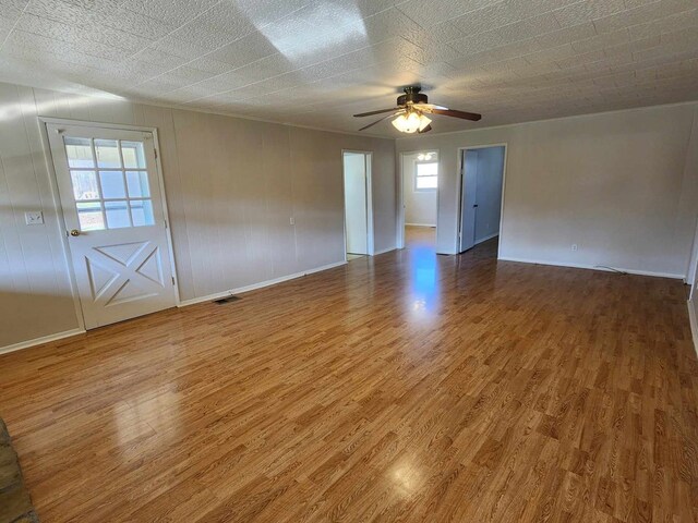 empty room with ceiling fan, wood finished floors, visible vents, and baseboards