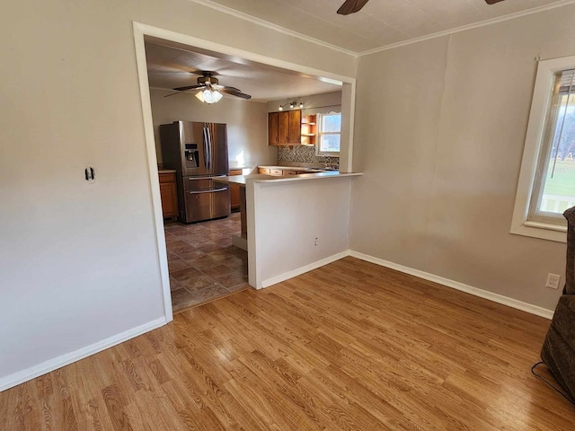 kitchen with tasteful backsplash, brown cabinetry, open floor plan, stainless steel fridge, and a peninsula