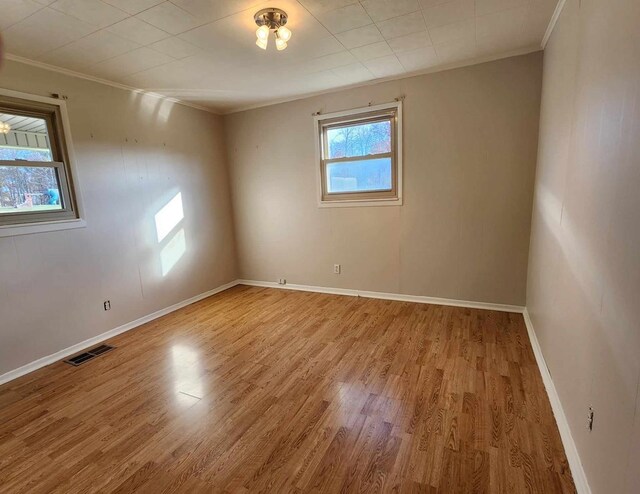 unfurnished room with baseboards, light wood-type flooring, visible vents, and crown molding