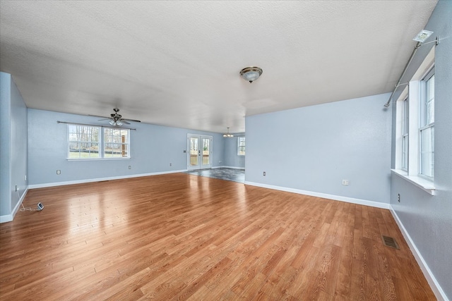 unfurnished living room featuring a wealth of natural light, visible vents, baseboards, and wood finished floors