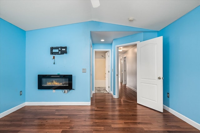 unfurnished bedroom featuring lofted ceiling, a glass covered fireplace, baseboards, and wood finished floors