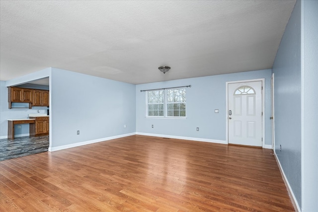 unfurnished living room with light wood-style floors, baseboards, and a textured ceiling