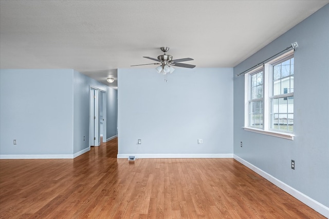 empty room with light wood finished floors, a ceiling fan, and baseboards