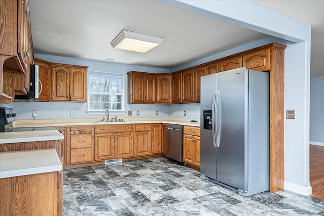 kitchen featuring stainless steel appliances, brown cabinetry, a sink, and visible vents