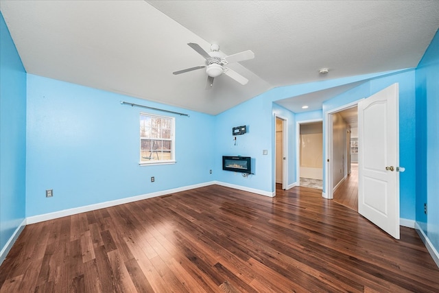 unfurnished living room featuring baseboards, a glass covered fireplace, ceiling fan, dark wood-type flooring, and vaulted ceiling